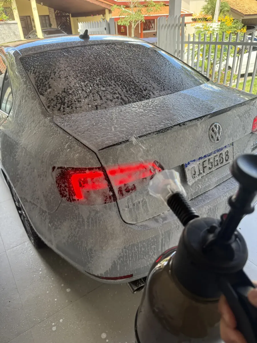 Traseira de um carro escuro coberta de espuma durante a lavagem